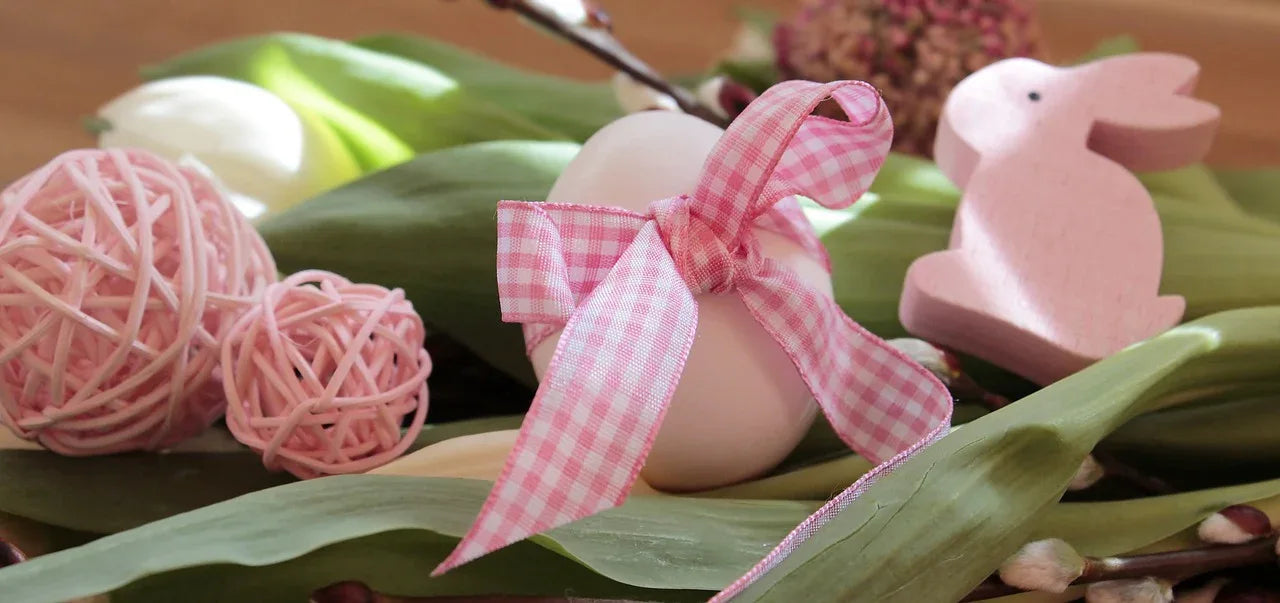 Easter Wear collection featuring a pink ribbon tied around an egg, surrounded by spring flowers and decorative wooden bunny. Perfect for celebrating Easter with style and joy.