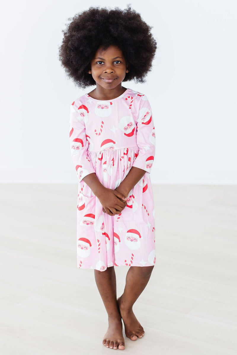 A young girl with natural hair wearing the pink Jingle Bells 3/4 Sleeve Pocket Twirl Dress featuring a playful Santa design, showcasing fun and charm during the holidays.