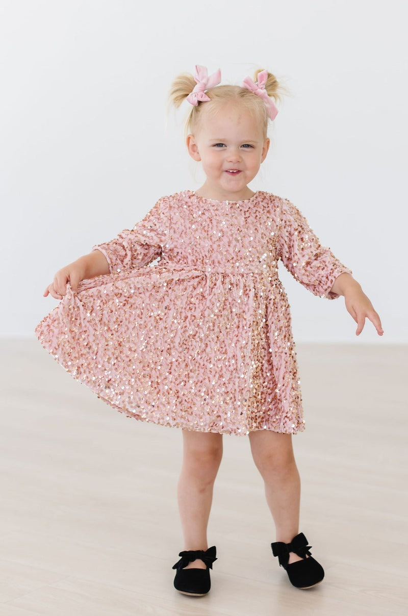 A happy toddler in a Rose Gold Velvet Sequin Dress from Mila & Rose, twirling and smiling, highlighting the dress's comfortable fit and dazzling sequins.