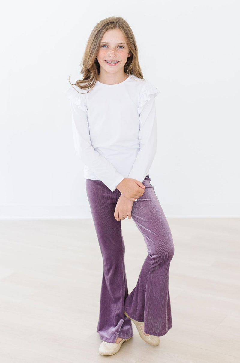A young girl in a ruffled white tee paired with Amethyst Ribbed Velvet Bells, displaying both comfort and trendy style for any casual occasion.