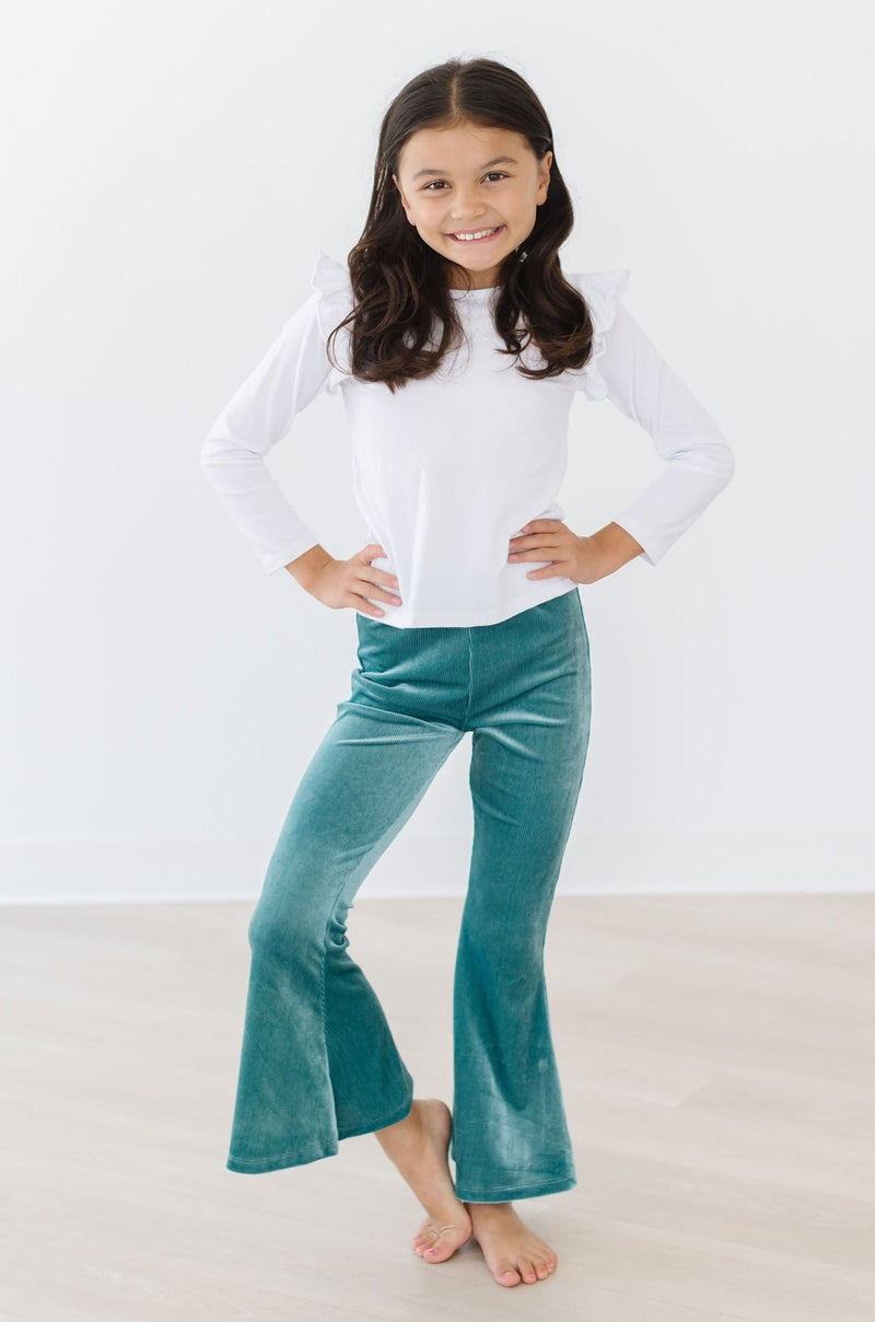Young girl posing confidently in Aquamarine Ribbed Velvet Bells paired with a white ruffle tee, highlighting the trendy and versatile style perfect for fall.