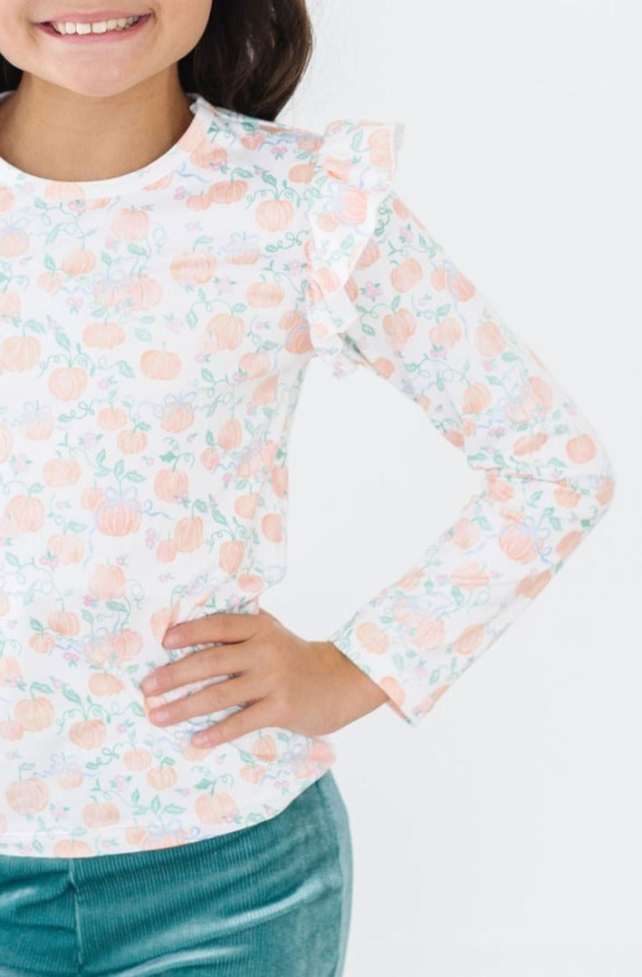 Pretty Pumpkins L/S Ruffle Tee showcasing a young girl smiling with ruffled sleeves, wearing a vibrant pumpkin print shirt.