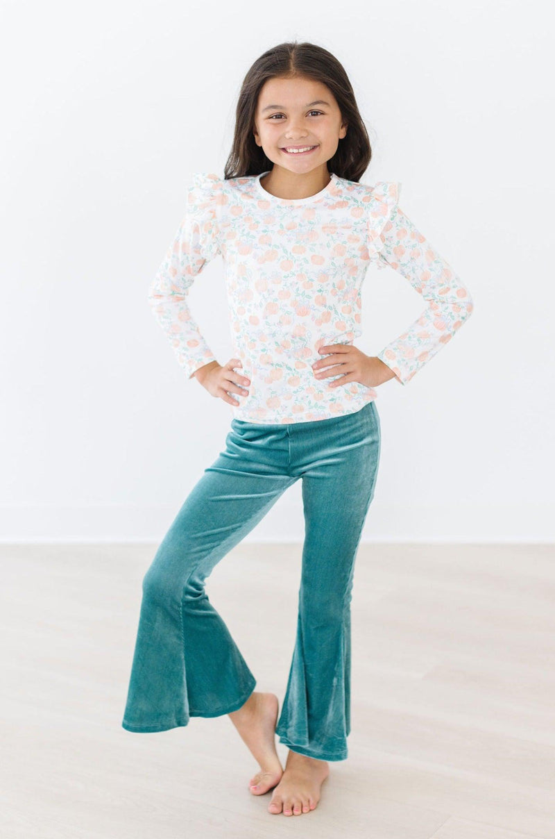 Pretty Pumpkins L/S Ruffle Tee worn by a happy girl posing with hands on her hips, paired with green flared pants.