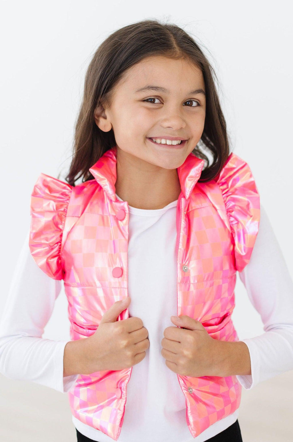 A cheerful young girl wearing the Neon Pink Checker Puffer Vest, showcasing its stylish ruffled shoulders and vibrant checker pattern, perfect for a trendy winter look.
