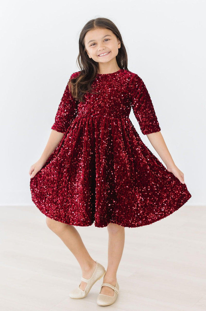Cheerful girl in a Cranberry Velvet Sequin Dress by Mila & Rose®, twirling to showcase the shimmering sequins and the dress's playful design.