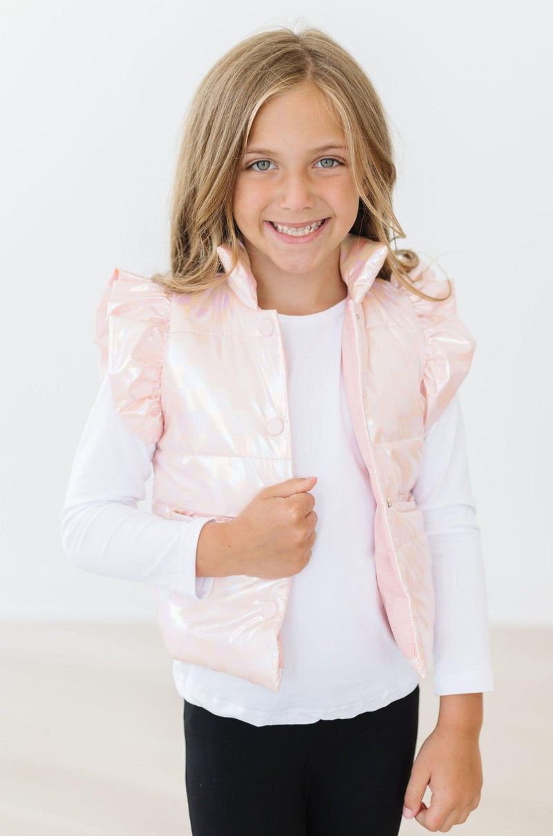 Smiling girl dons a stylish Light Pink Checker Puffer Vest over a white long-sleeve tee, radiating warmth and cheer in a light-toned room.