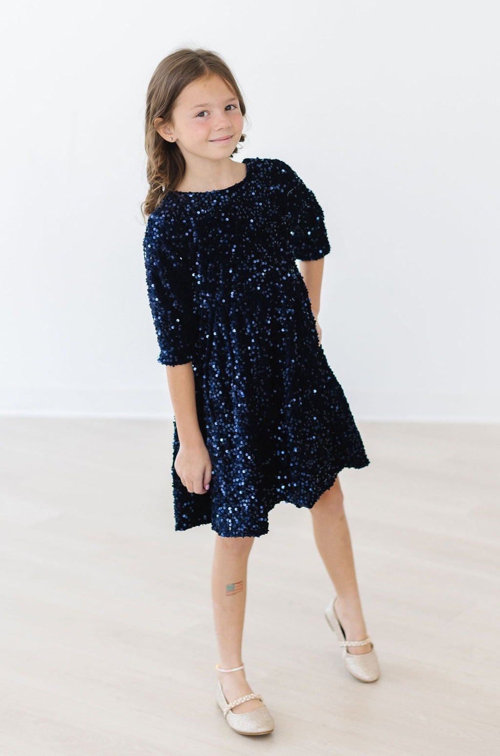 A young girl showcasing the Navy Velvet Sequin Dress by Mila & Rose®, featuring its sparkling sequins and soft velvet texture in a playful pose.