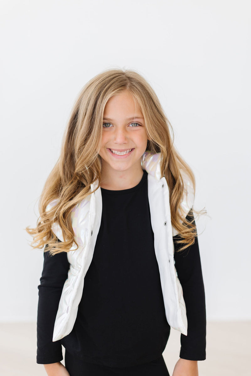 A young girl smiling while wearing the White Checker Puffer Vest, showcasing its stylish design against a plain white background.
