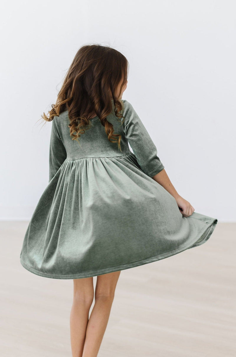 Sage Velvet Twirl Dress by Mila & Rose®, showcasing a girl twirling in a beautiful green velvet dress with elegant details, ideal for special occasions.