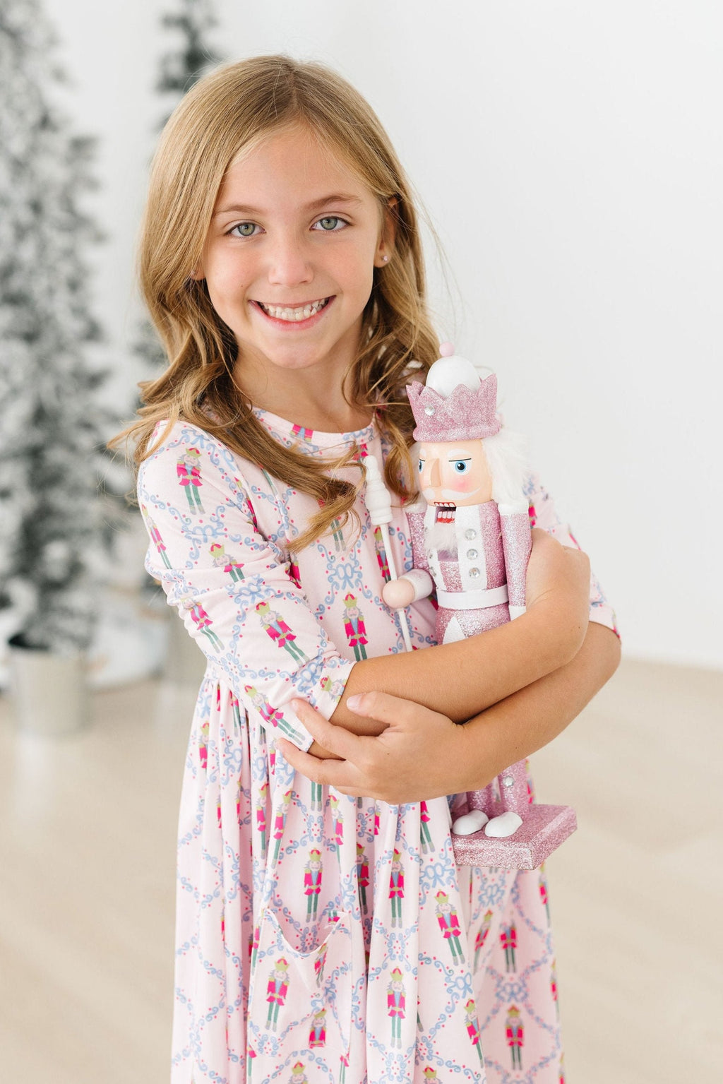 Delightful Pink Nutcracker 3/4 Sleeve Pocket Twirl Dress worn by a smiling girl holding a nutcracker doll, perfect for festive occasions.