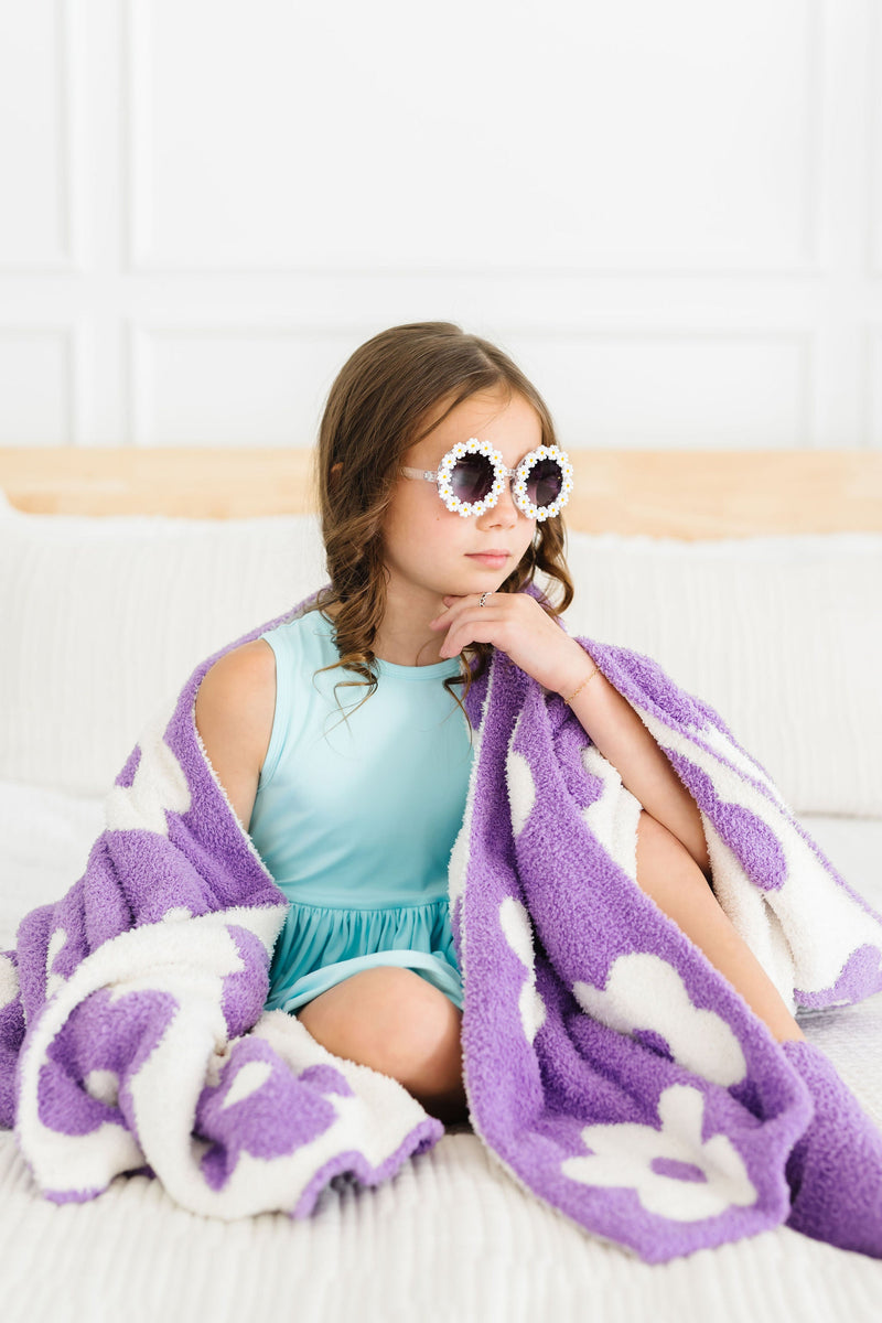 Fashionable girl seated on a bed, wrapped in the Lilac/Coconut Flower Cozy Blanket, radiating comfort and sophistication.