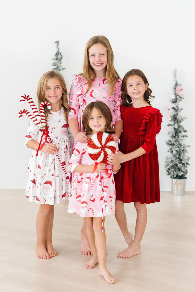 Four girls joyfully posing in their Jingle Bells 3/4 Sleeve Pocket Twirl Dresses, showcasing a festive theme with Santa prints and red accents, ideal for holiday fun.