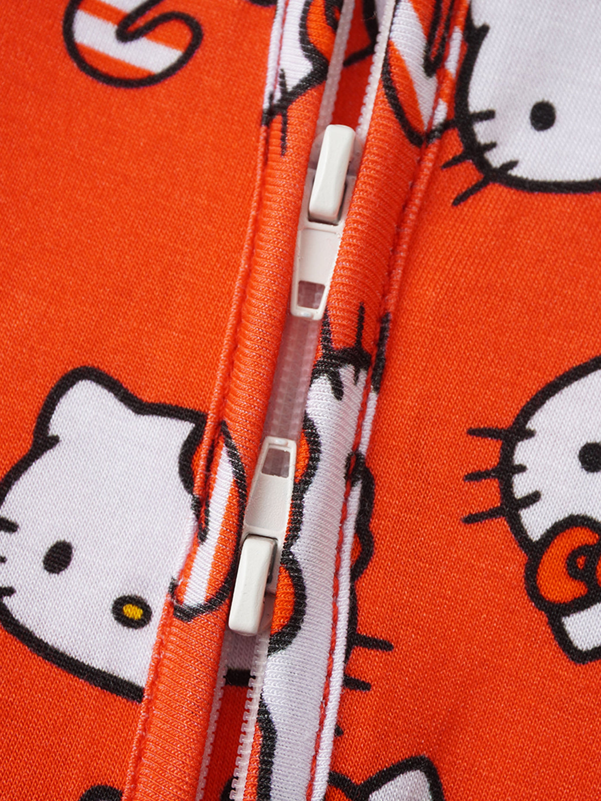 Extreme close-up of white plastic double zipper slider tabs and protective placket on orange romper.