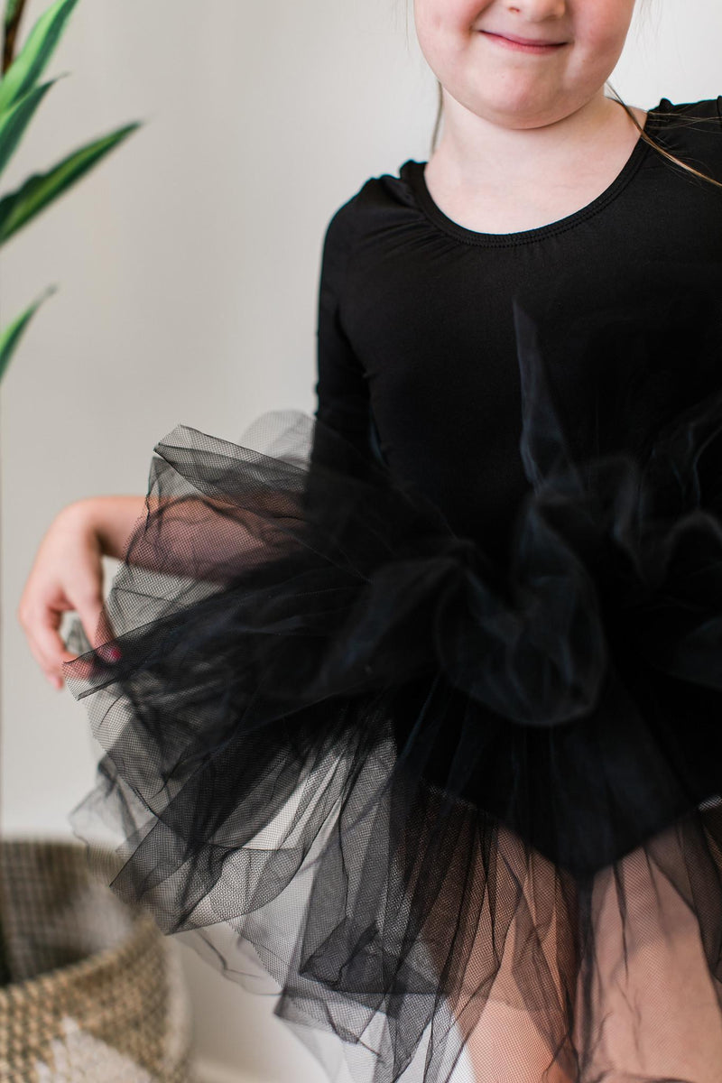 Close-up of a child in a Black 3/4 Tutu Leotard by Mila & Rose, showcasing the fluffy tulle layers and playful design while smiling gracefully.