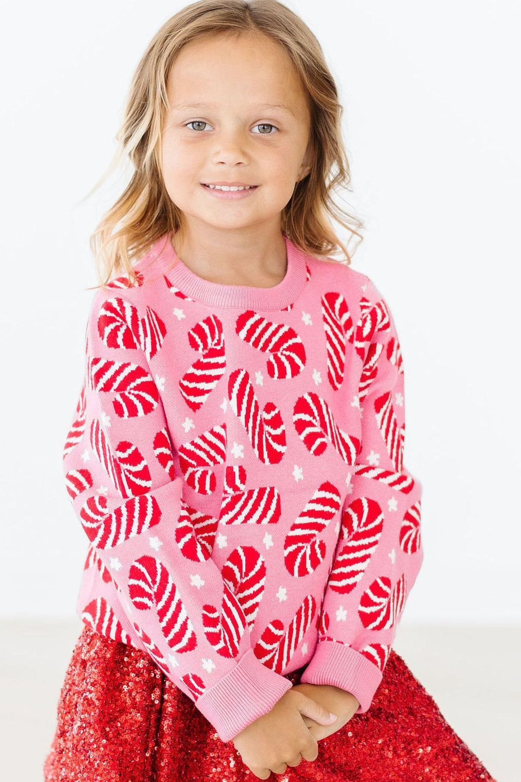 A cheerful child wearing the Candy Canes Sweater from Mila & Rose, featuring a playful candy cane design in vibrant colors, paired with a sparkly red skirt, perfect for holiday festivities.
