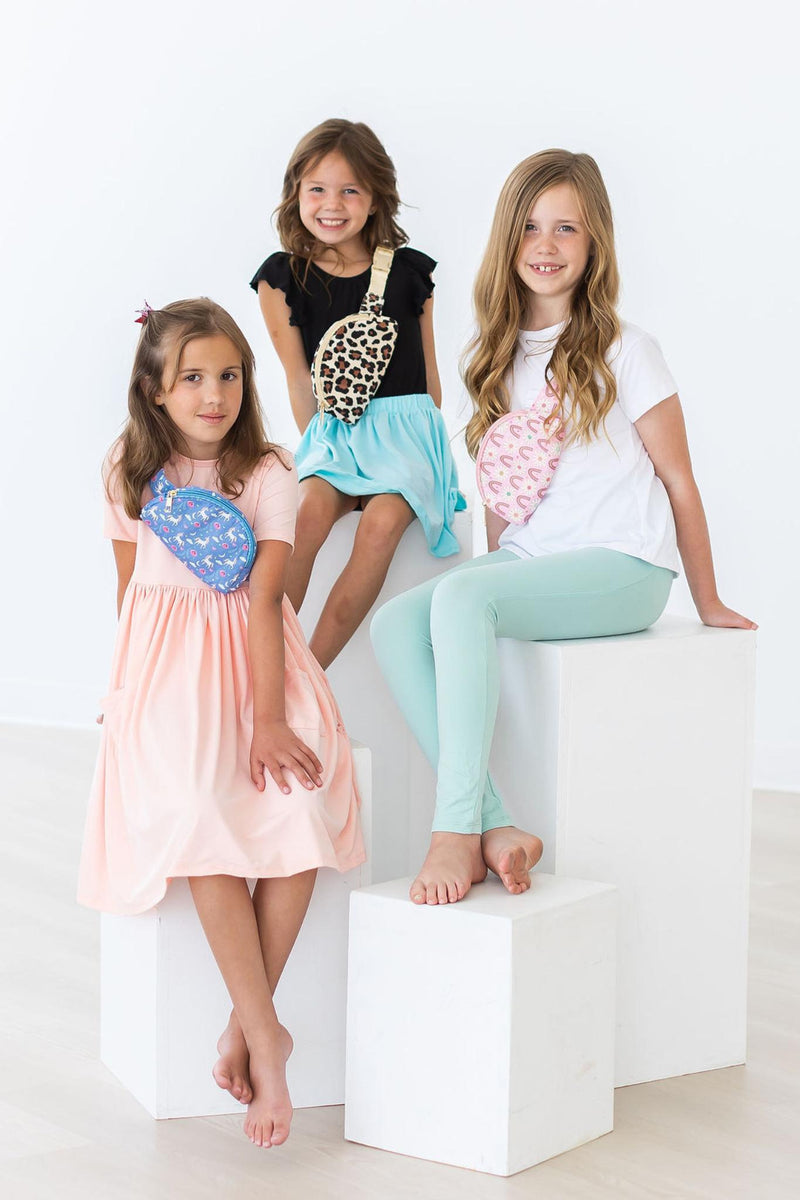 Three young girls modeled with the Blue Moon Belt Bag by Mila & Rose, showcasing stylish outfits and the playful design of the bag in a bright, cheerful setting.