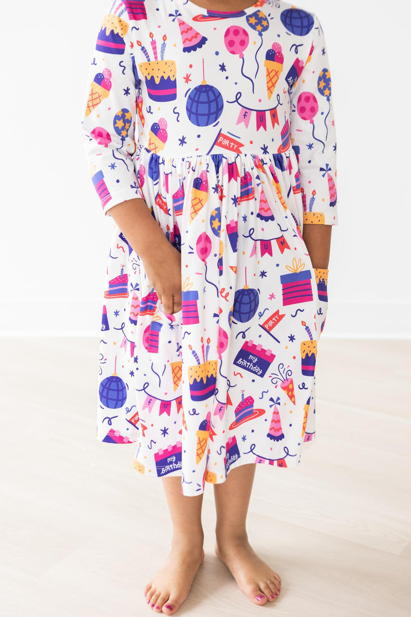 Happy Birthday 3/4 Sleeve Pocket Twirl Dress showcasing a joyful girl with hands in pockets, featuring vibrant birthday-themed patterns.