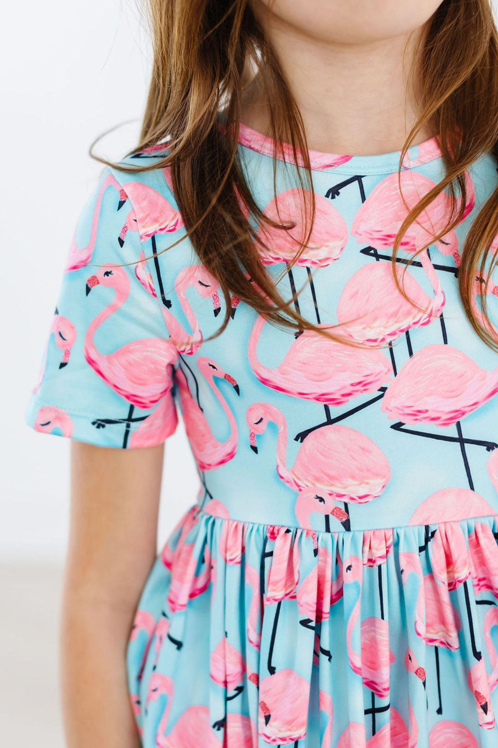 Close-up of a girl wearing the Pretty in Pink Flamingos S/S Pocket Twirl Dress, showcasing vibrant flamingo patterns and a cheerful style.