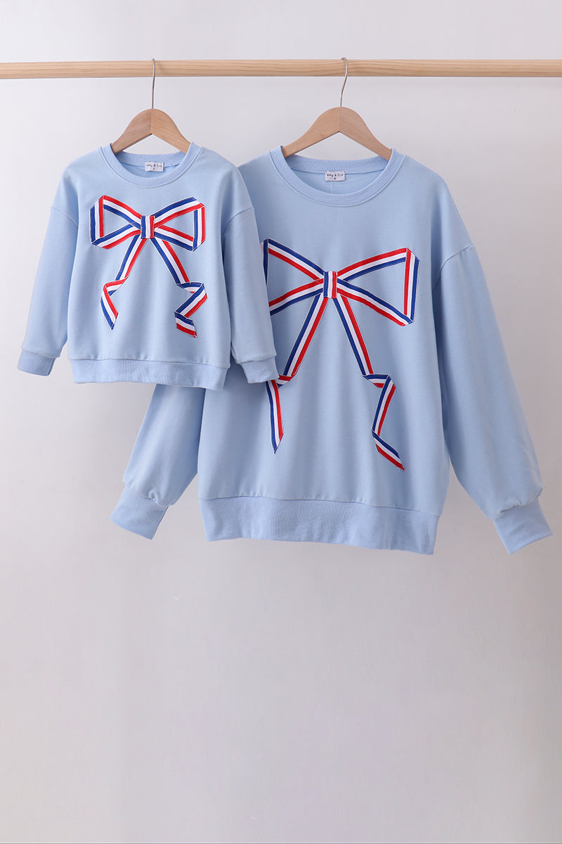 Two light blue sweatshirts with red and blue bow designs on a white background.