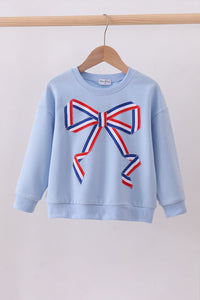 Light blue sweatshirt with a large red, white, and blue bow design on a wooden hanger against a light gray background.