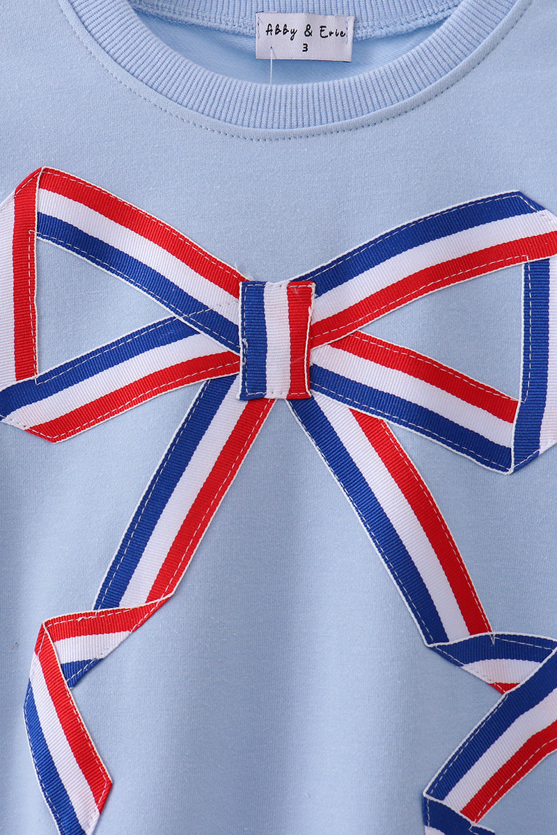 Light blue sweater with a large red, white, and blue bow on a light blue background