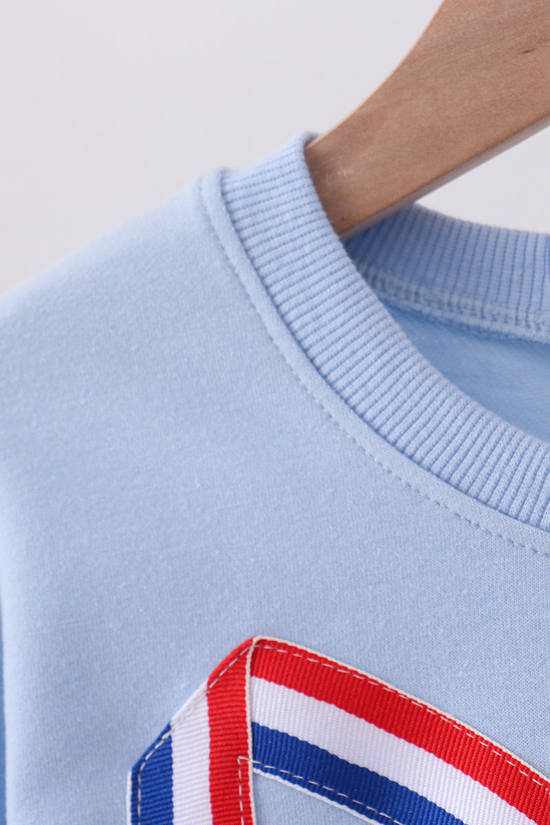 Light blue sweater with a red, white, and blue striped detail on a neutral background