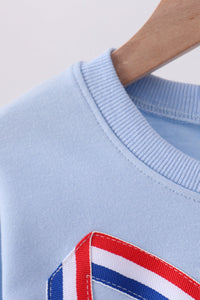 Light blue sweater with a red, white, and blue striped detail on a neutral background