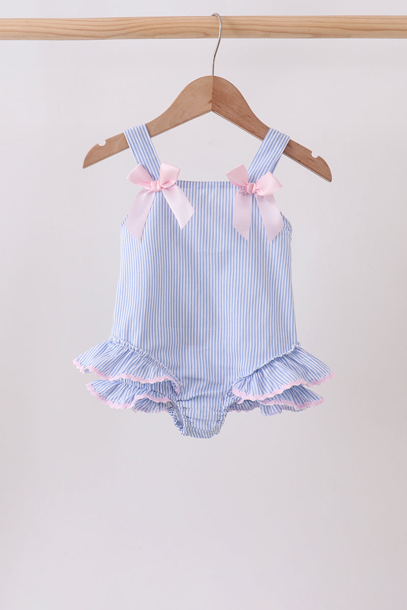Blue and white striped baby romper with ruffles and pink bows on a hanger against a beige background