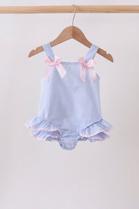 Blue and white striped baby romper with ruffles and pink bows on a hanger against a beige background