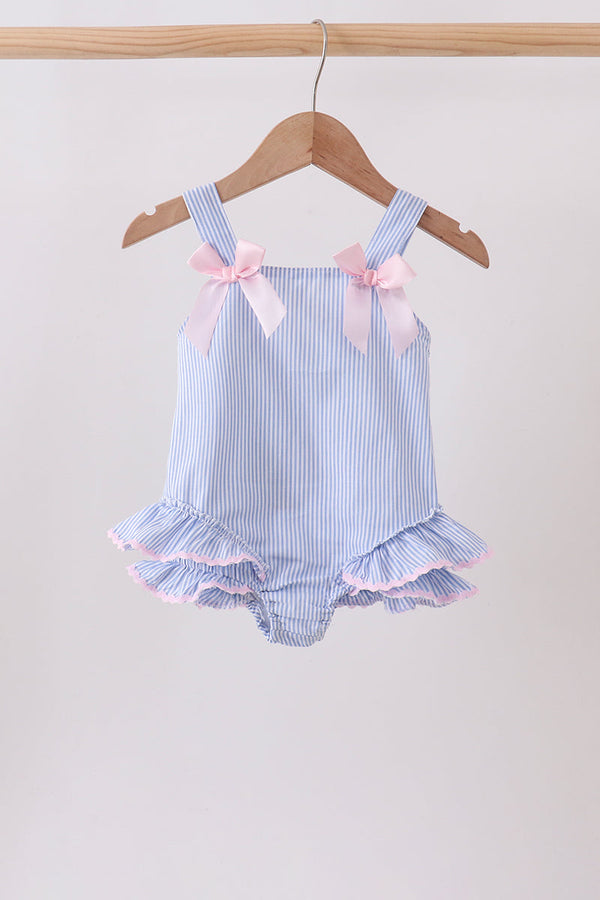 Blue and white striped baby romper with ruffles and pink bows on a hanger against a beige background