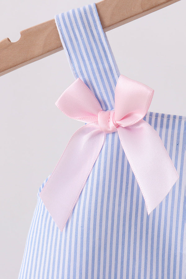 Blue and white striped dress with a pink bow on a wooden hanger against a light background