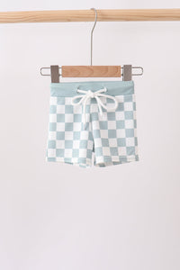 Checkered shorts with a tie waist hanging on a wooden hanger against a white background