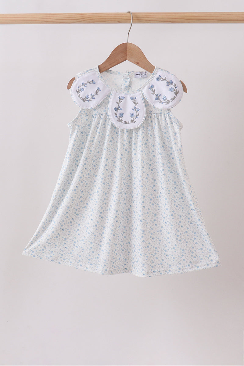 White dress with floral embroidery on a wooden hanger against a beige background