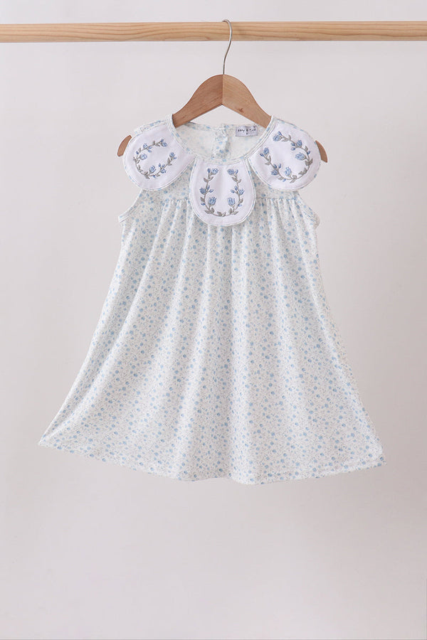 White dress with floral embroidery on a wooden hanger against a beige background