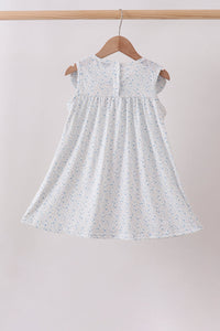 White dress with subtle pattern on a wooden hanger against a plain background