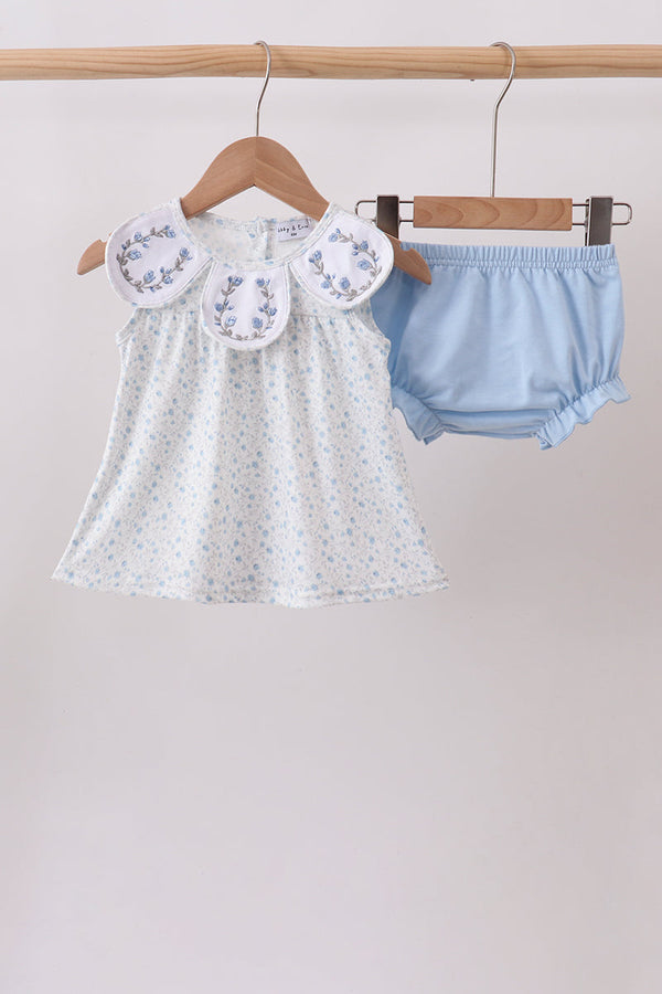 Baby dress and bloomers on hangers against a plain background