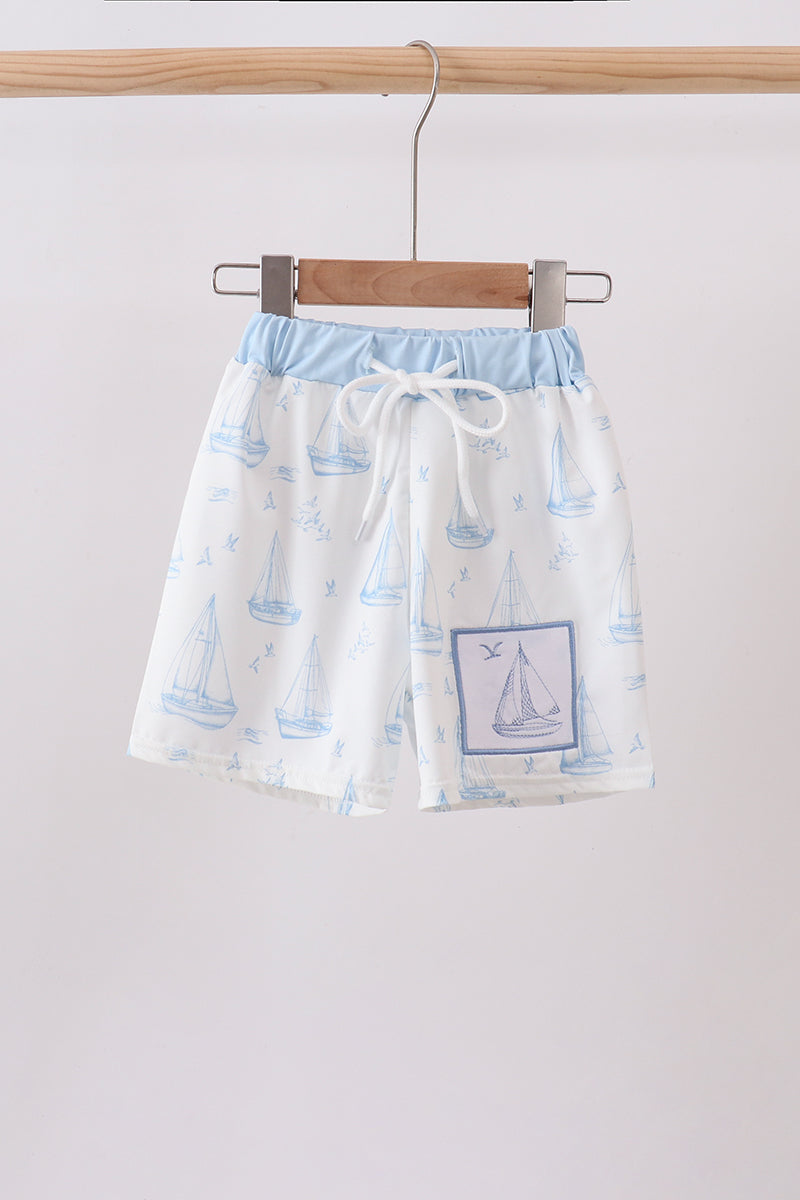 White swim trunks with blue sailboat embroidery patch and light blue waistband.