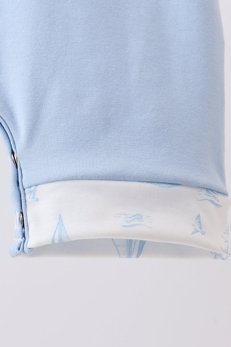 Close-up of a light blue garment with a folded cuff showing a white lining printed with light blue nautical sailboat motifs.