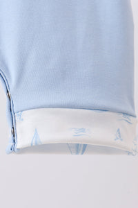 Close-up of a light blue garment with a folded cuff showing a white lining printed with light blue nautical sailboat motifs.