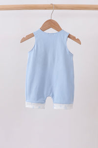 A light blue sleeveless baby romper hanging on a wooden hanger from a wooden clothes rack against a plain light background.