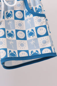A close-up of a children's tank top or swimsuit sleeve featuring a blue and white checkerboard pattern with crabs, palm trees, suns, and smiley faces.