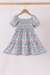Blue floral smocked ruffle dress for girls with puffed sleeves and delicate bodice detailing on a wooden hanger.