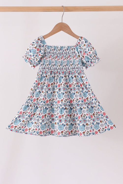 Blue floral smocked ruffle dress for girls with puffed sleeves and delicate bodice detailing on a wooden hanger.