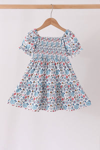 Blue floral girls dress with smocked bodice, ruffled sleeves, and tiered hem hanging on a wooden hanger.