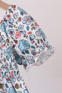 Blue floral girls dress featuring delicate smocked bodice detailing and a ruffled puff sleeve with soft pink and red accents on a white background.