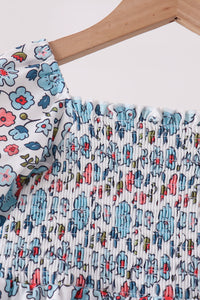 Blue floral smocked bodice on a girls' dress with elastic gathering detail and colorful blossom print on white fabric.