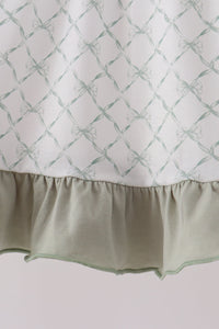 Sage green dress fabric features a bow lattice pattern above a soft, gathered ruffle hem.