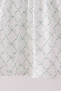 White fabric featuring a sage green lattice pattern with small bows, showcasing the ruffled hem detail of a bloomer set.