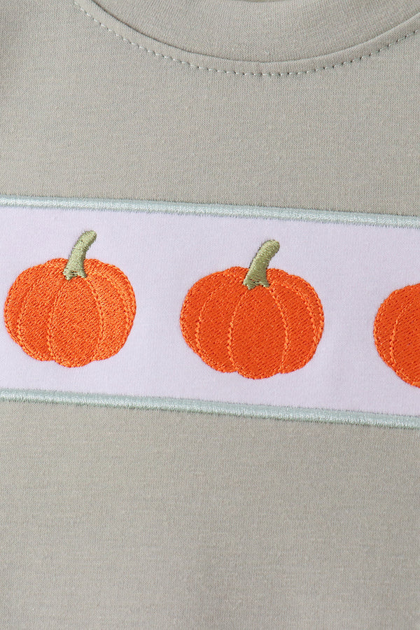 Close-up of sage green fabric with orange pumpkin embroidery on a white band, perfect for fall shorts sets.