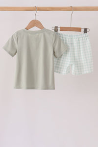 Back view of sage green shorts set with solid tee and gingham shorts hanging on wooden hanger.